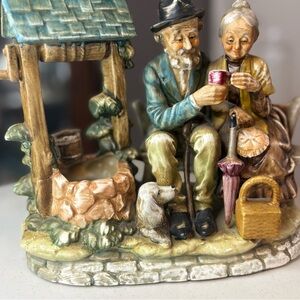 Charming figurine of old man and woman sitting at the well with their dog